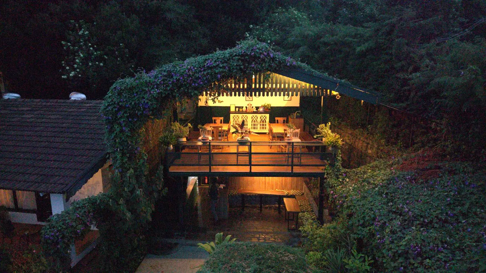 The restaurant deck glowing at blue hour under an arch of flowering creeper