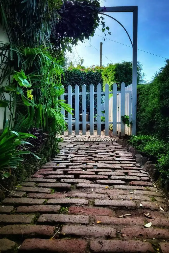 A brick path through the garden to a white picket gate